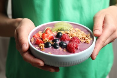 Woman holding bowl with tasty acai smoothie and fruits on blurred background, closeup