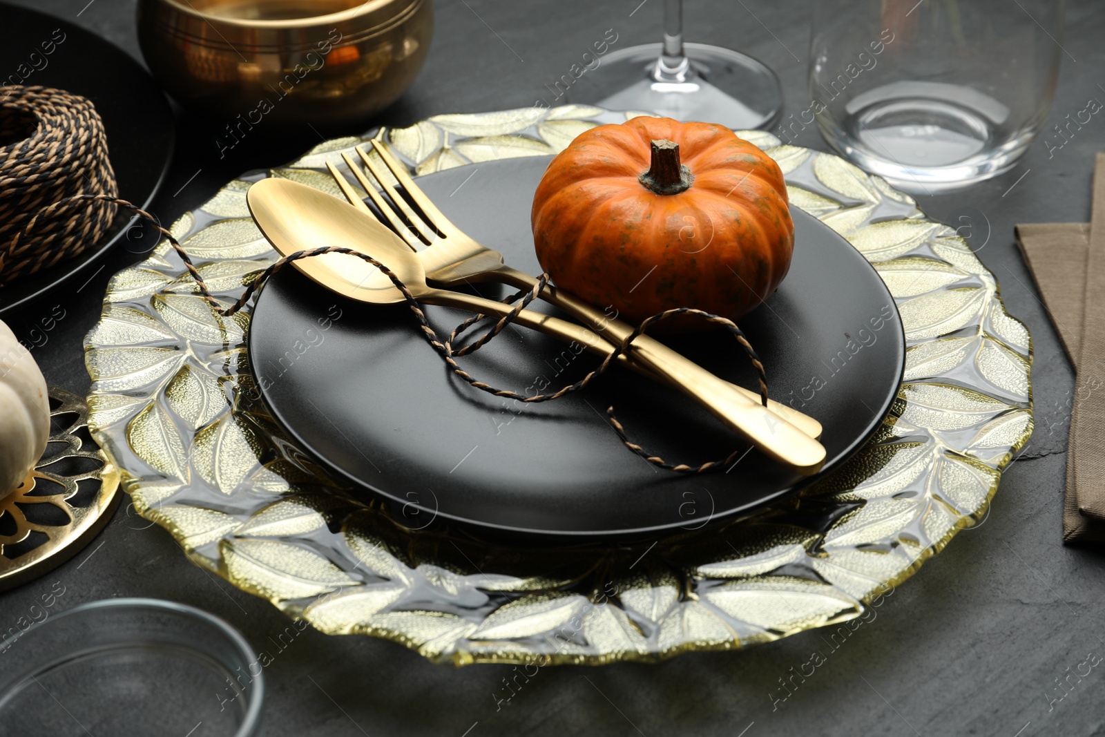 Photo of Autumn table setting with golden cutlery and pumpkin on black background