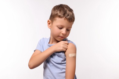 Boy with sticking plaster on arm after vaccination against white background