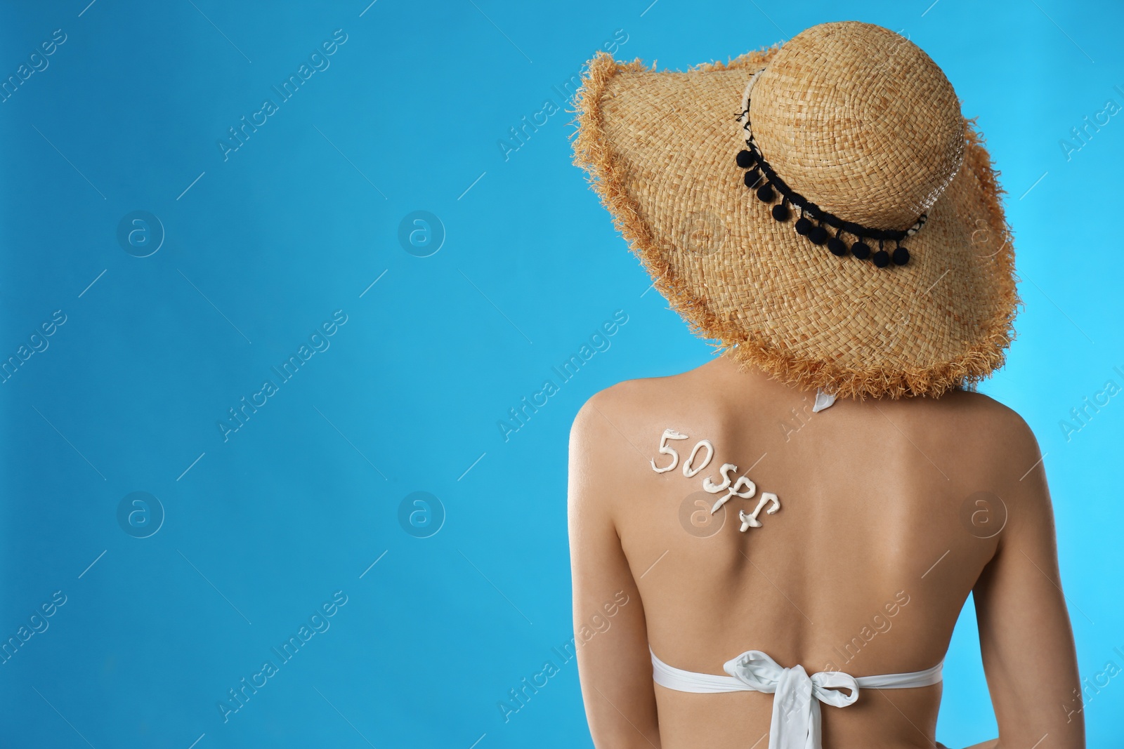 Photo of 50 SPF written with sun protection cream on woman's back against light blue background. Space for text