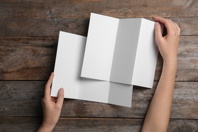Photo of Woman with blank brochures on wooden background, above view. Mock up for design