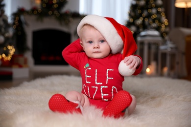 Photo of Cute little baby in red bodysuit and Santa hat on floor at home. Christmas suit