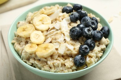 Tasty oatmeal with banana, blueberries, coconut flakes and honey served in bowl on beige table, closeup