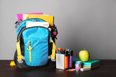 Children's backpack and different school stationery on wooden table against grey background