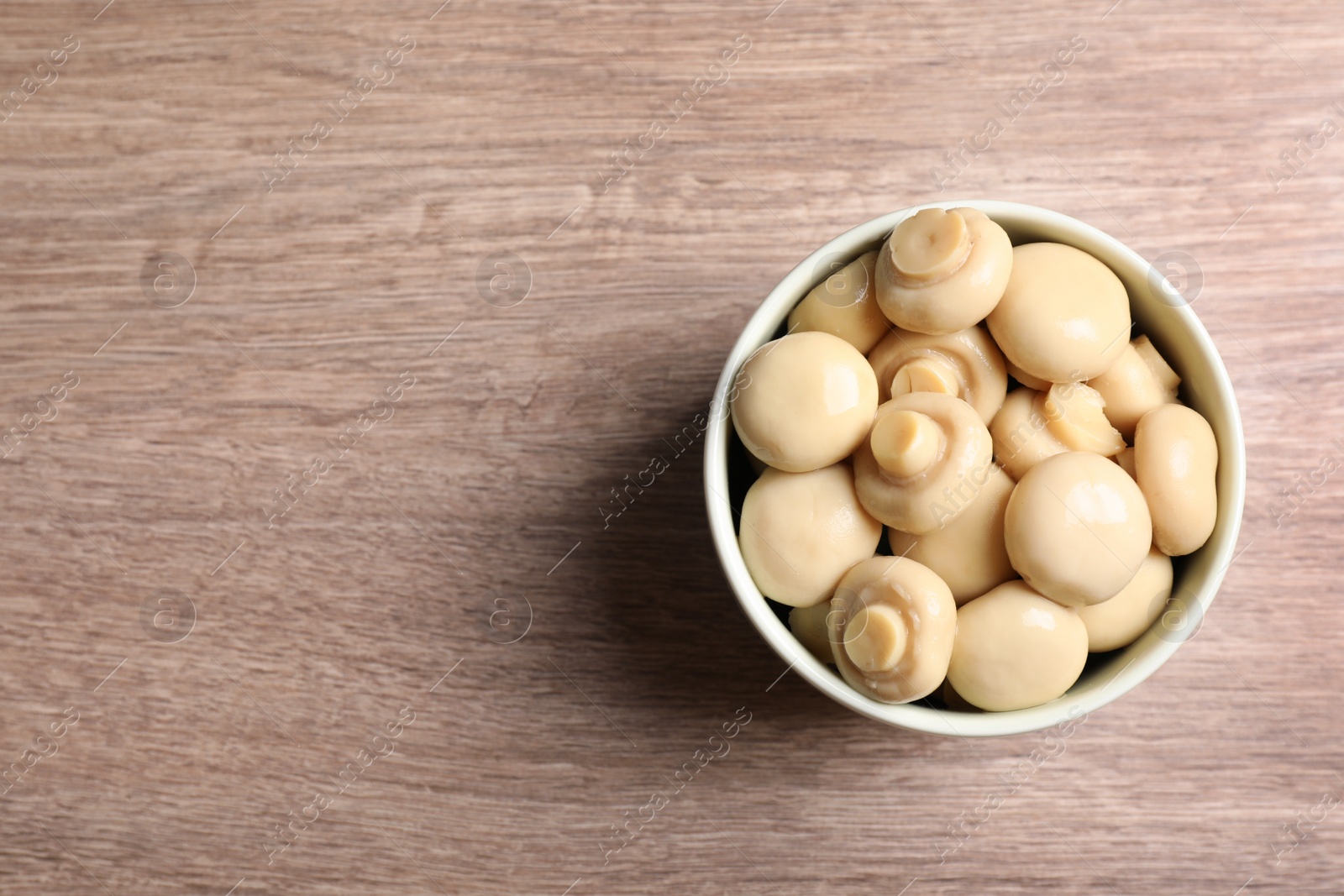 Photo of Delicious marinated mushrooms in bowl on wooden table, top view. Space for text