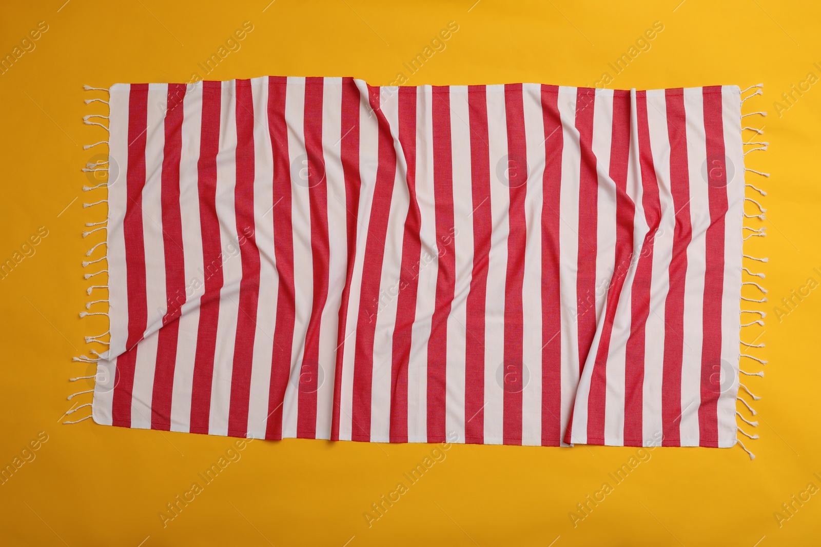 Photo of Crumpled striped beach towel on yellow background, top view