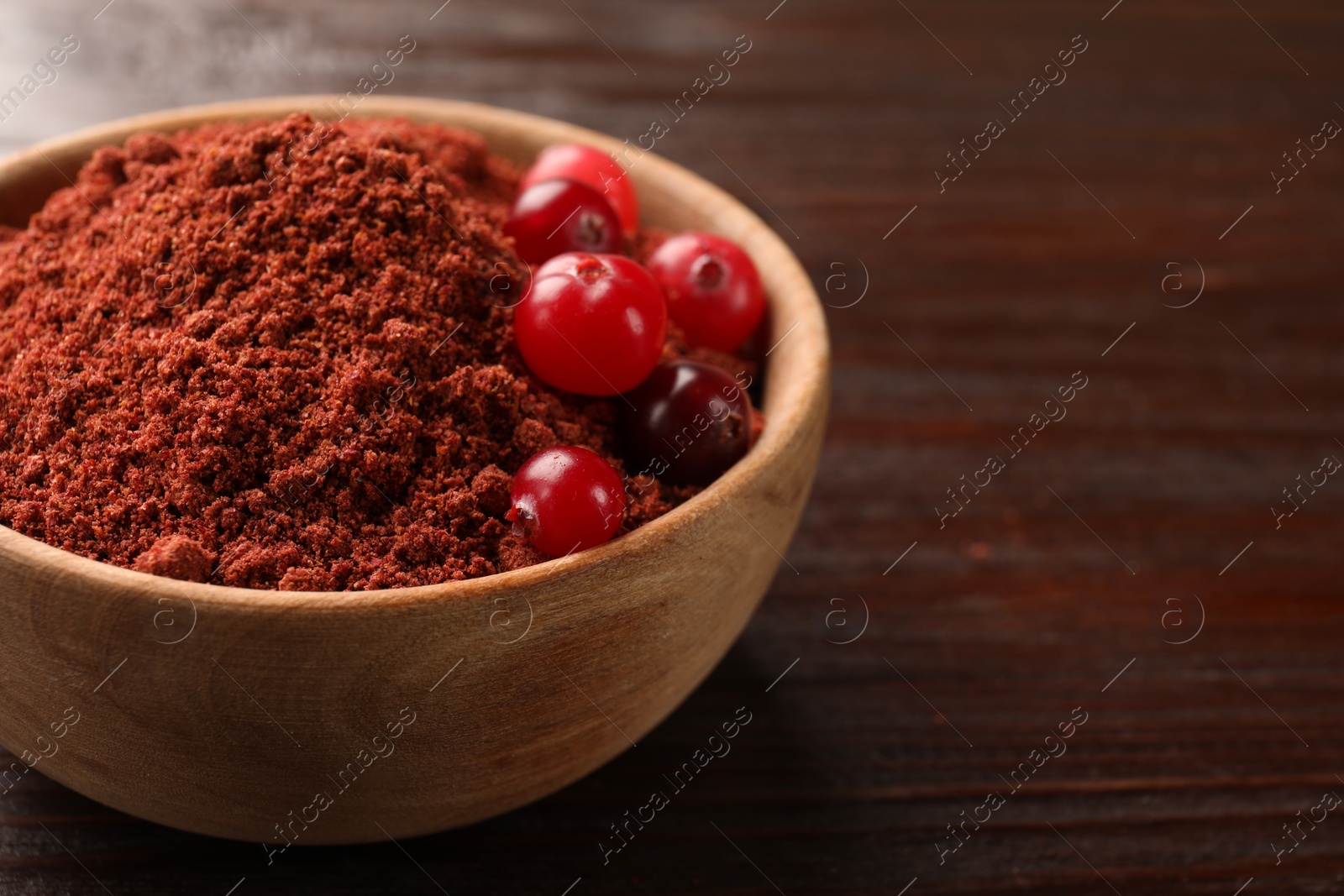 Photo of Dried cranberry powder and fresh berries in bowl on wooden table, closeup. Space for text