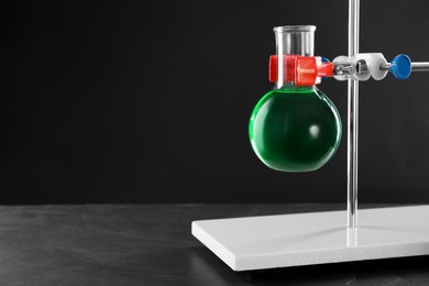 Photo of Retort stand and laboratory flask with liquid on table against black background, closeup. Space for text