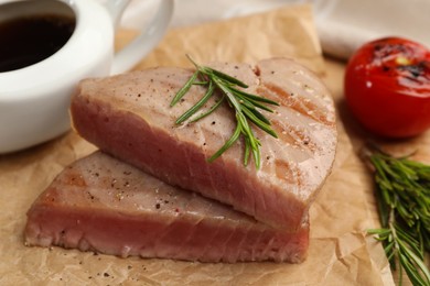 Photo of Pieces of delicious tuna with rosemary on parchment paper, closeup