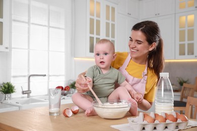 Photo of Happy young woman and her cute little baby making dough together in kitchen, space for text