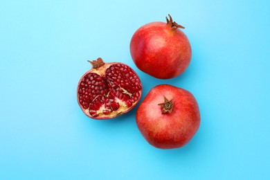 Photo of Whole and cut fresh pomegranates on light blue background, flat lay