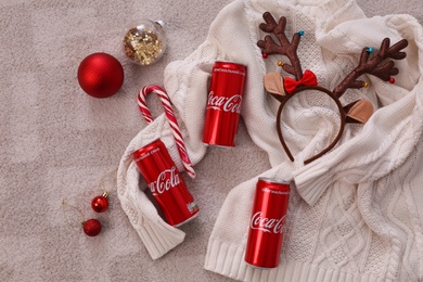 Photo of MYKOLAIV, UKRAINE - JANUARY 13, 2021: Flat lay composition with Coca-Cola cans, Christmas decor and sweater on floor