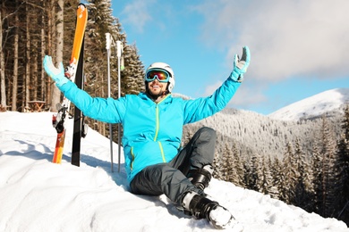 Photo of Man with ski equipment sitting on snow in mountains. Winter vacation