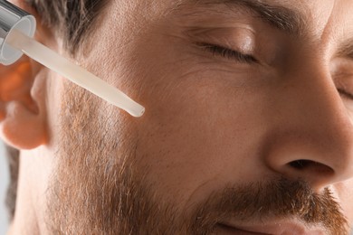 Photo of Handsome man applying cosmetic serum onto his face, closeup