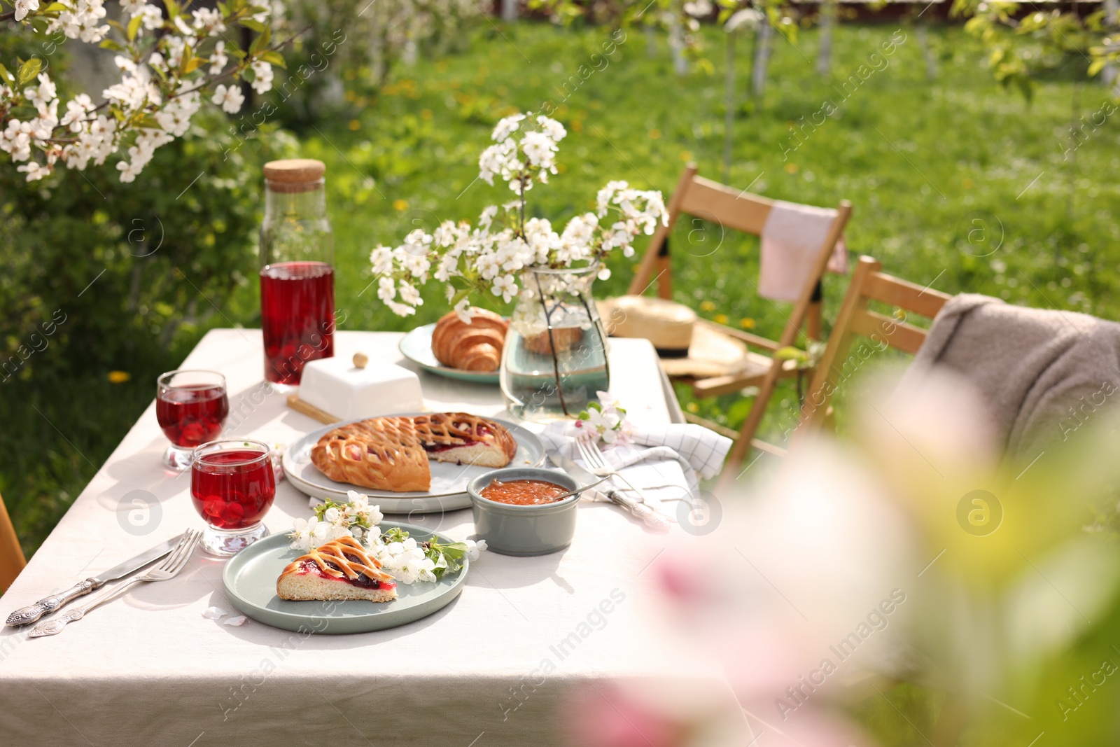 Photo of Stylish table setting with beautiful spring flowers, fruit drink and pie in garden