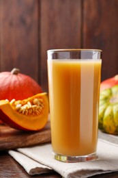 Photo of Tasty pumpkin juice in glass and different pumpkins on wooden table