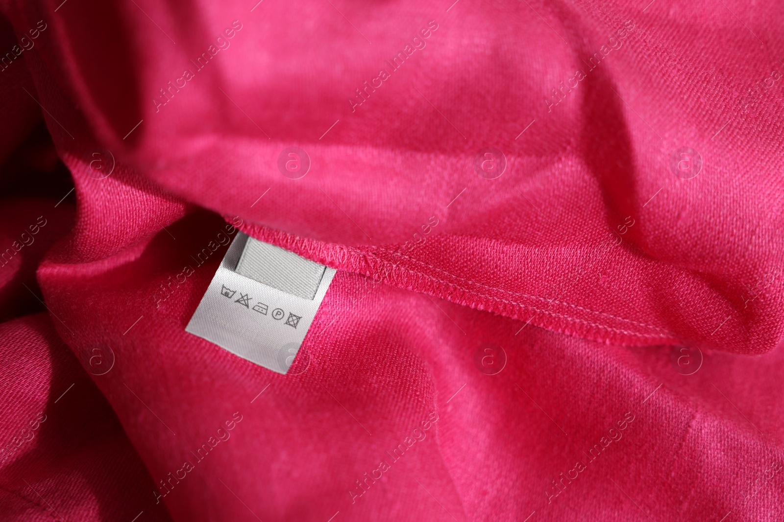 Photo of Clothing label in different languages on pink garment, closeup