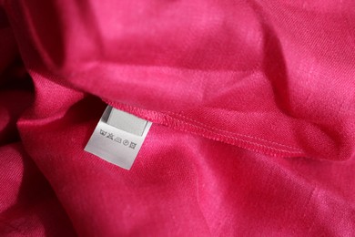 Photo of Clothing label in different languages on pink garment, closeup