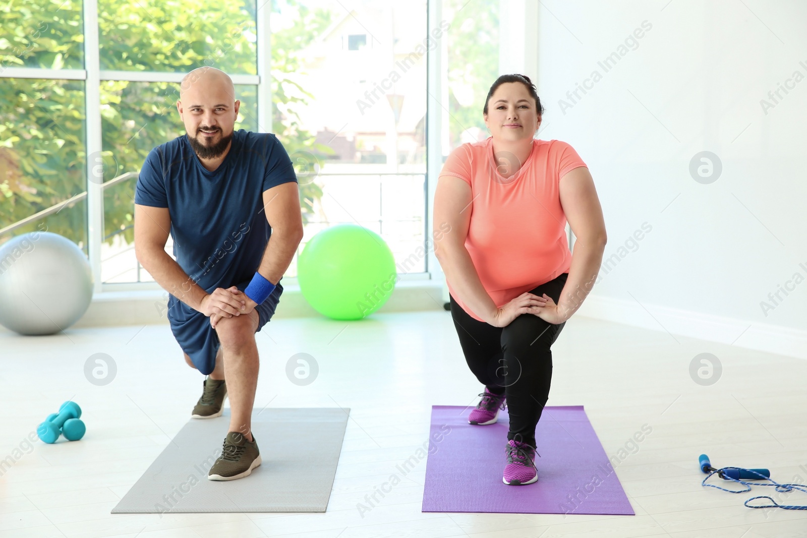 Photo of Overweight man and woman doing exercise on mats in gym