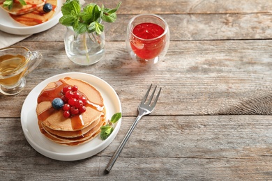 Stack of tasty pancakes with berries and syrup on table