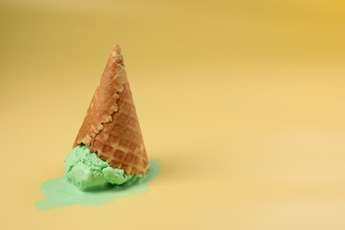 Photo of Melted ice cream in wafer cone on pale yellow background. Space for text