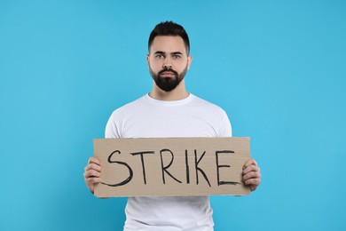 Photo of Man holding cardboard banner with word Strike on light blue background