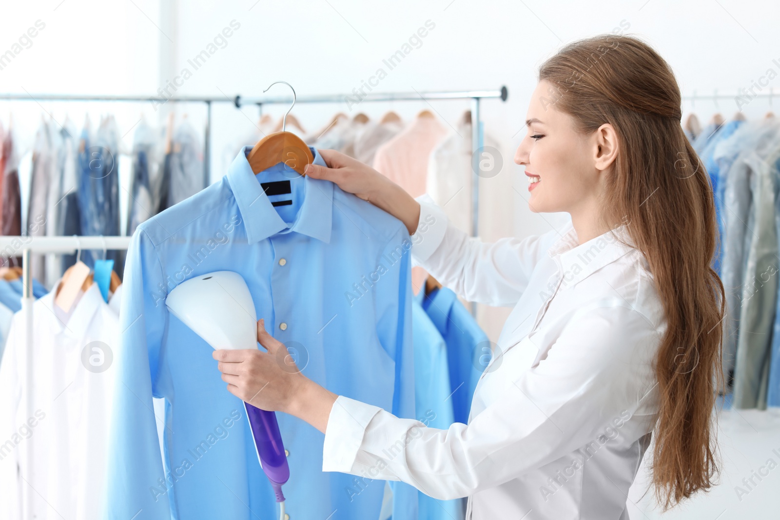 Photo of Young woman steaming shirt at dry-cleaner's