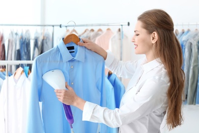 Young woman steaming shirt at dry-cleaner's