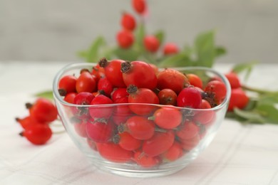 Photo of Ripe rose hip berries in bowl on white table, closeup