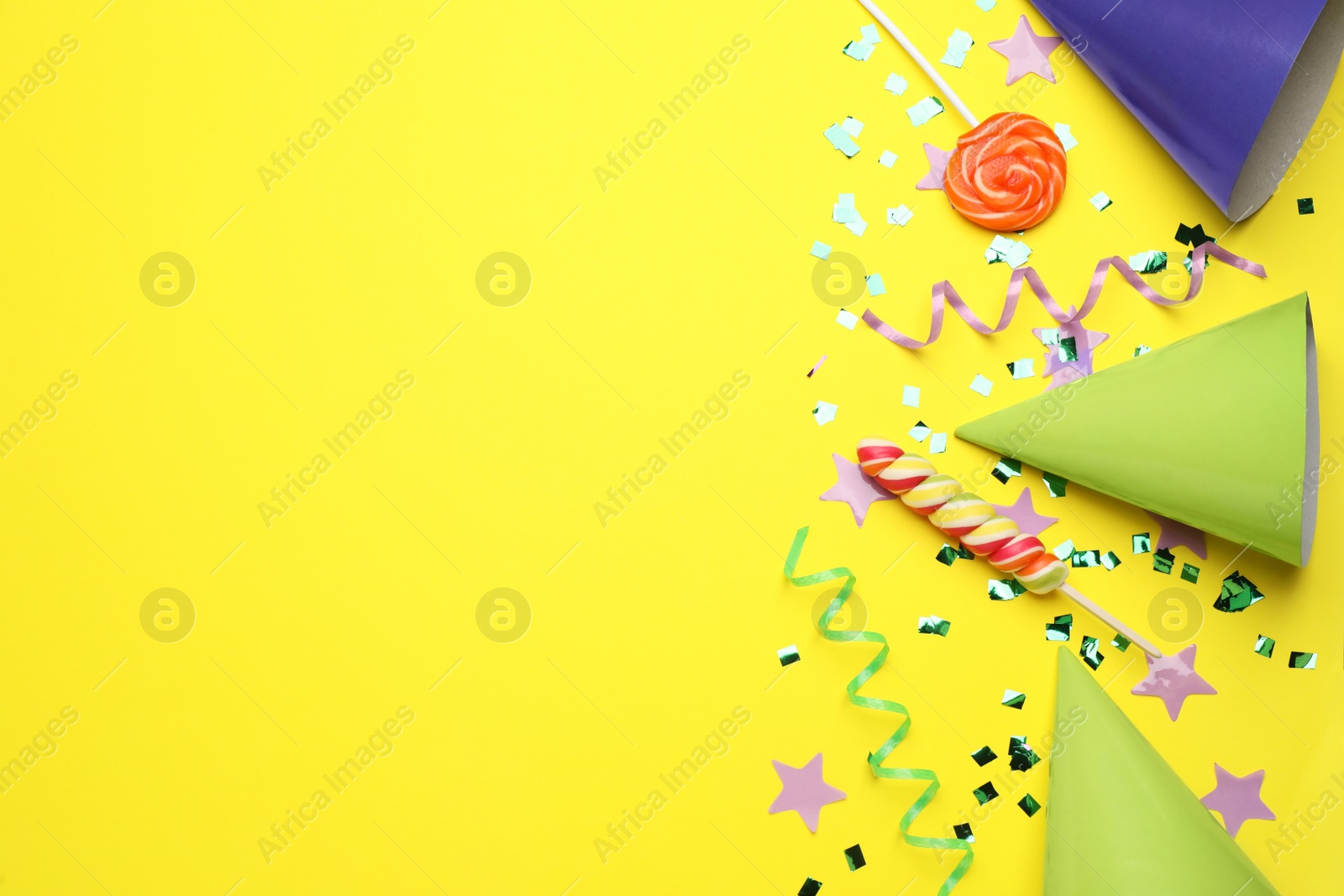 Photo of Flat lay composition with party hats and other festive items on yellow background, space for text. Birthday surprise