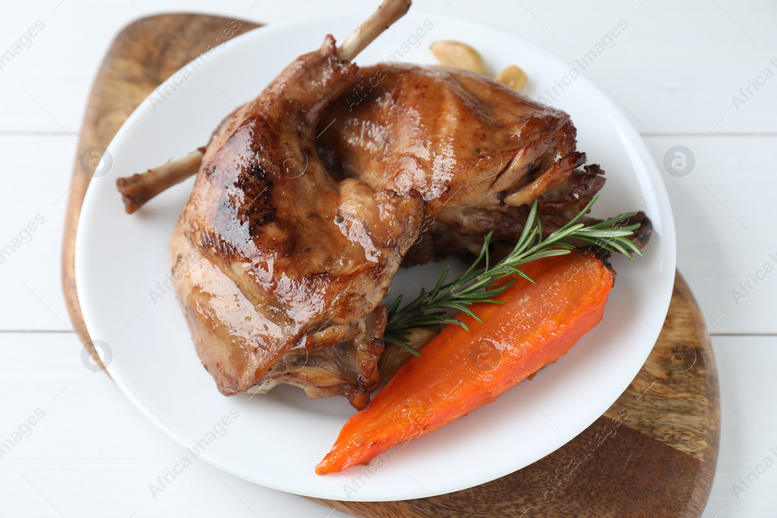 Photo of Tasty cooked rabbit meat with rosemary, garlic and carrot on white wooden table, above view