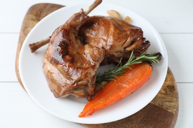 Photo of Tasty cooked rabbit meat with rosemary, garlic and carrot on white wooden table, above view