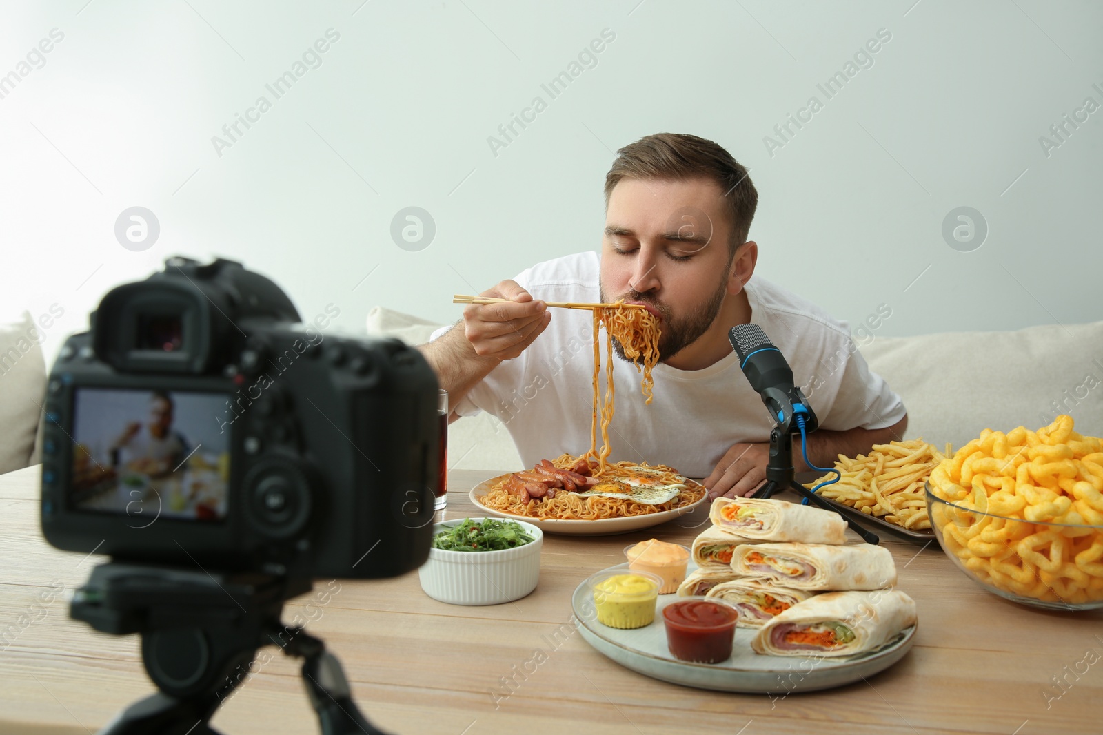 Photo of Food blogger recording eating show on camera against light background. Mukbang vlog