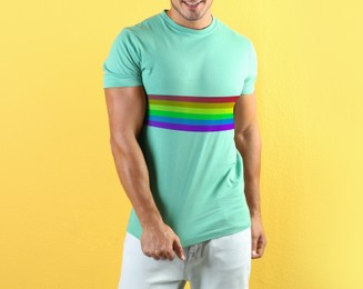Image of Young man wearing turquoise t-shirt with image of LGBT pride flag on yellow background