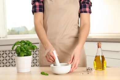 Photo of Woman grinding fresh basil in mortar while cooking at home, closeup