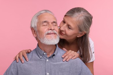 Photo of Senior woman kissing her beloved man on pink background