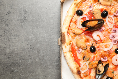 Delicious seafood pizza in box on grey table, top view. Space for text