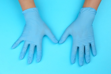 Photo of Person in latex gloves against light blue background, closeup on hands