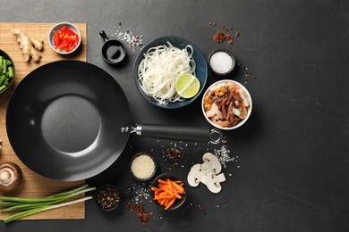 Photo of Flat lay composition with black wok, spices and products on dark textured table. Space for text