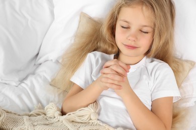 Girl with clasped hands praying in bed