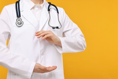 Doctor with stethoscope holding something on orange background, closeup. Space for text