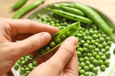 Photo of Woman shelling green peas over plate, closeup