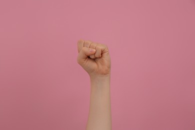 Photo of Woman raising fist on pink background, closeup
