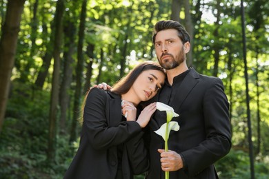 Photo of Sad couple with white calla lily flower mourning outdoors. Funeral ceremony