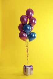 Bright balloons and gift box on color background