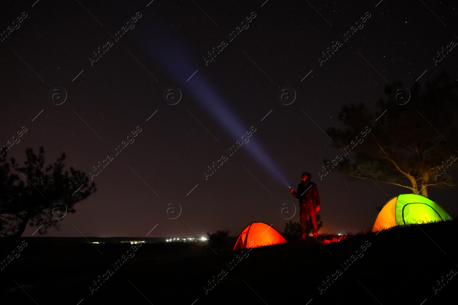 Photo of Man with bright flashlight near camping tents outdoors at night