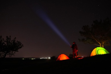 Photo of Man with bright flashlight near camping tents outdoors at night