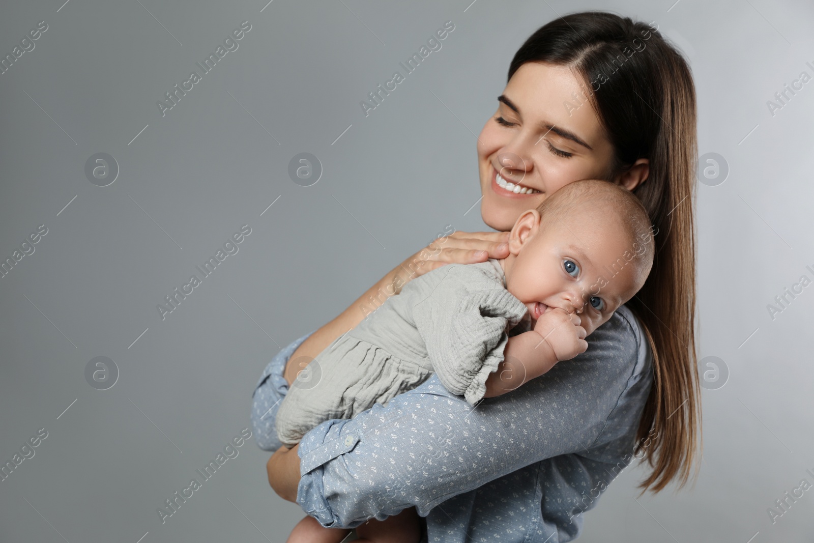 Photo of Beautiful mother with her cute baby on grey background. Space for text