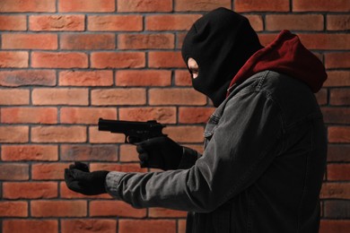 Photo of Dangerous criminal with gun near brick wall. Armed robbery