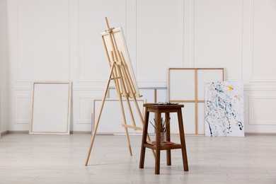 Photo of Wooden easel with canvas and painting supplies in artist's studio